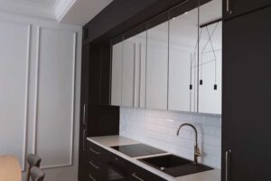 Grafitová kuchyňská linka s bílým obkladem a zrcadlovými horními skříňkami, které opticky zvětšují prostor.