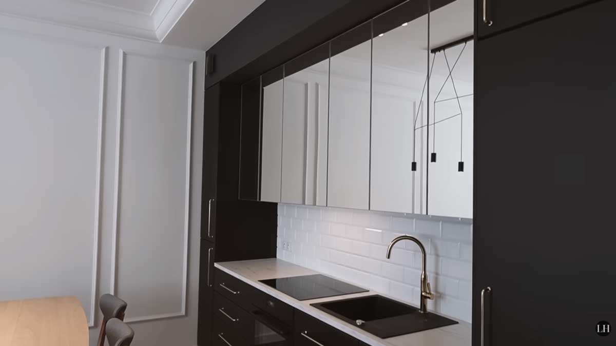 Grafitová kuchyňská linka s bílým obkladem a zrcadlovými horními skříňkami, které opticky zvětšují prostor.