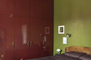 Ložnice s vintage dřevěnou postelí olivově zelenou stěnou a velkou bordó vestavěnou skříní.