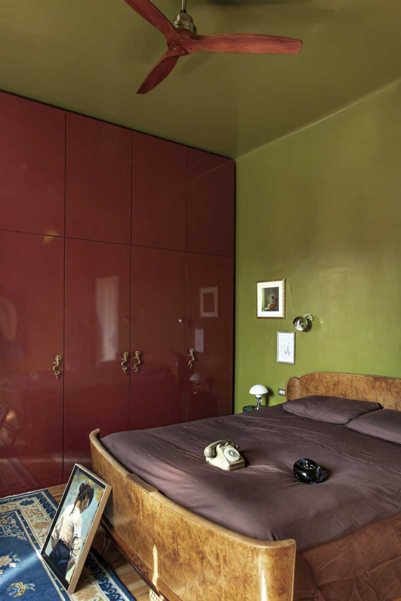 Ložnice s vintage dřevěnou postelí olivově zelenou stěnou a velkou bordó vestavěnou skříní.