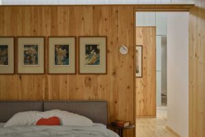 Ložnice s dřevěným obkladem, jednoduchou postelí a galerií obrazů nad čelem