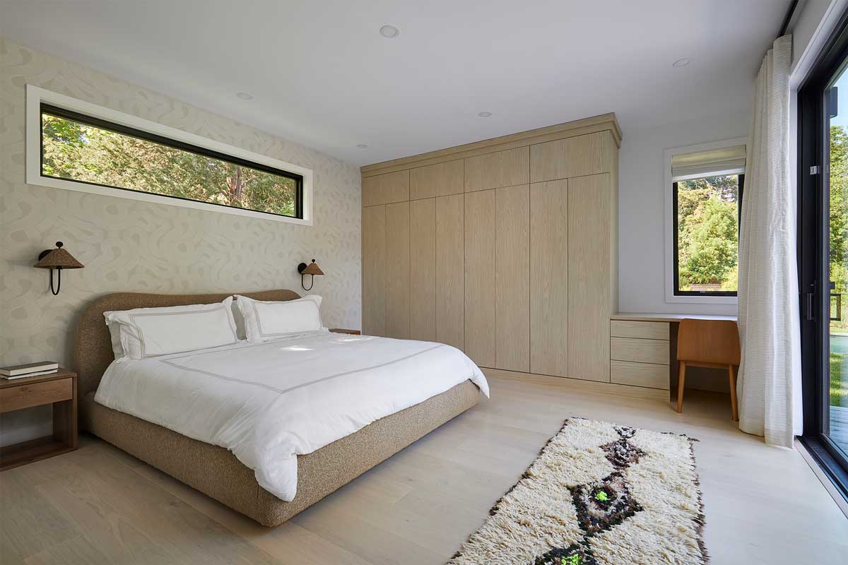 Světlá ložnice s vestavěnou skříní, přírodními materiály a výhledem do zahrady působí klidně a harmonicky.