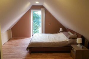 Minimalistická ložnice v podkroví se šikmým stropem a velkým oknem