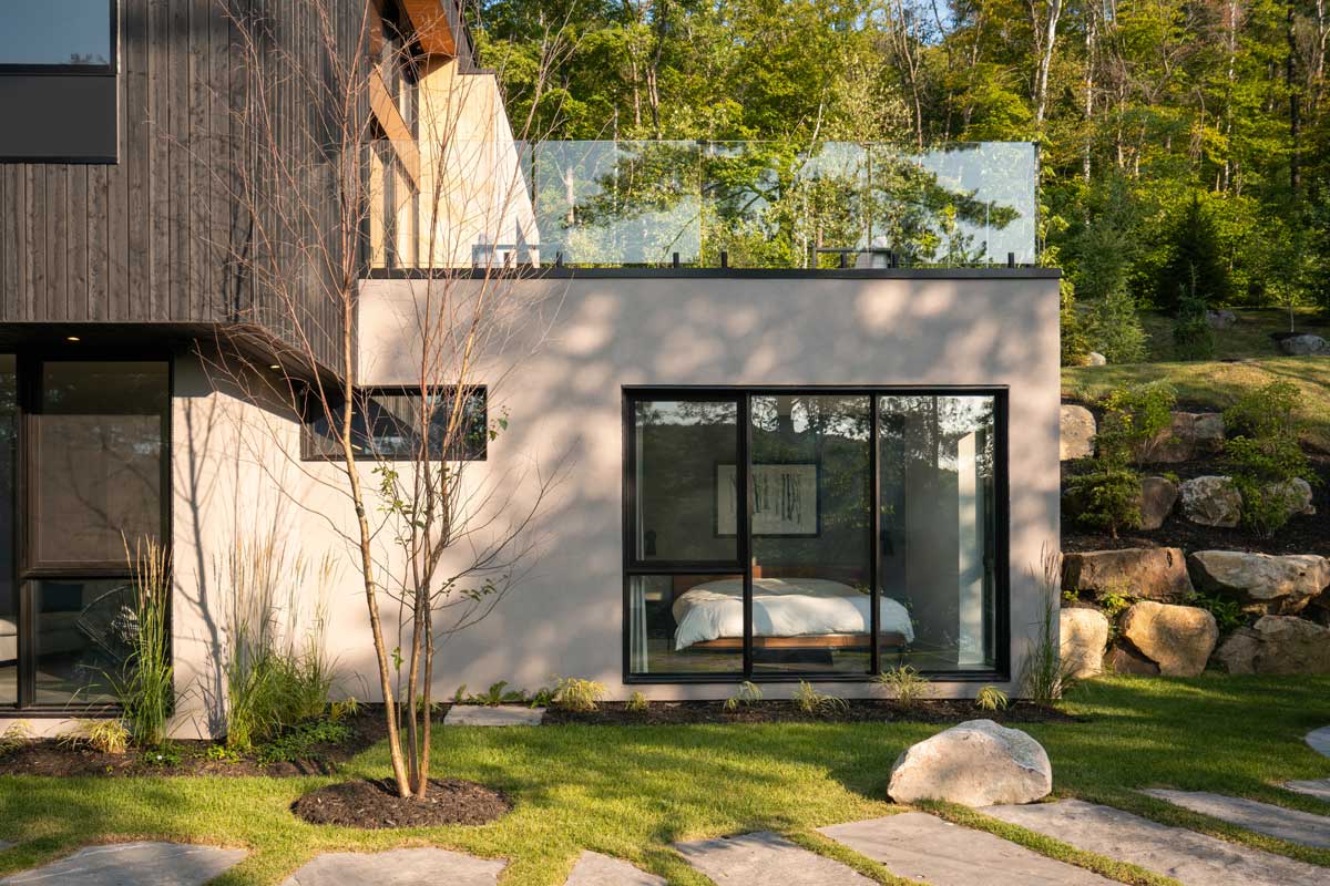 Pohled na ložnici z exteriéru se zapuštěným podlažím ve svahu a velkým oknem.