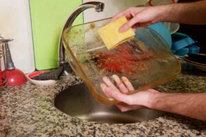 Ruční oplachování zapékací mísy před vložením do myčky nádobí.