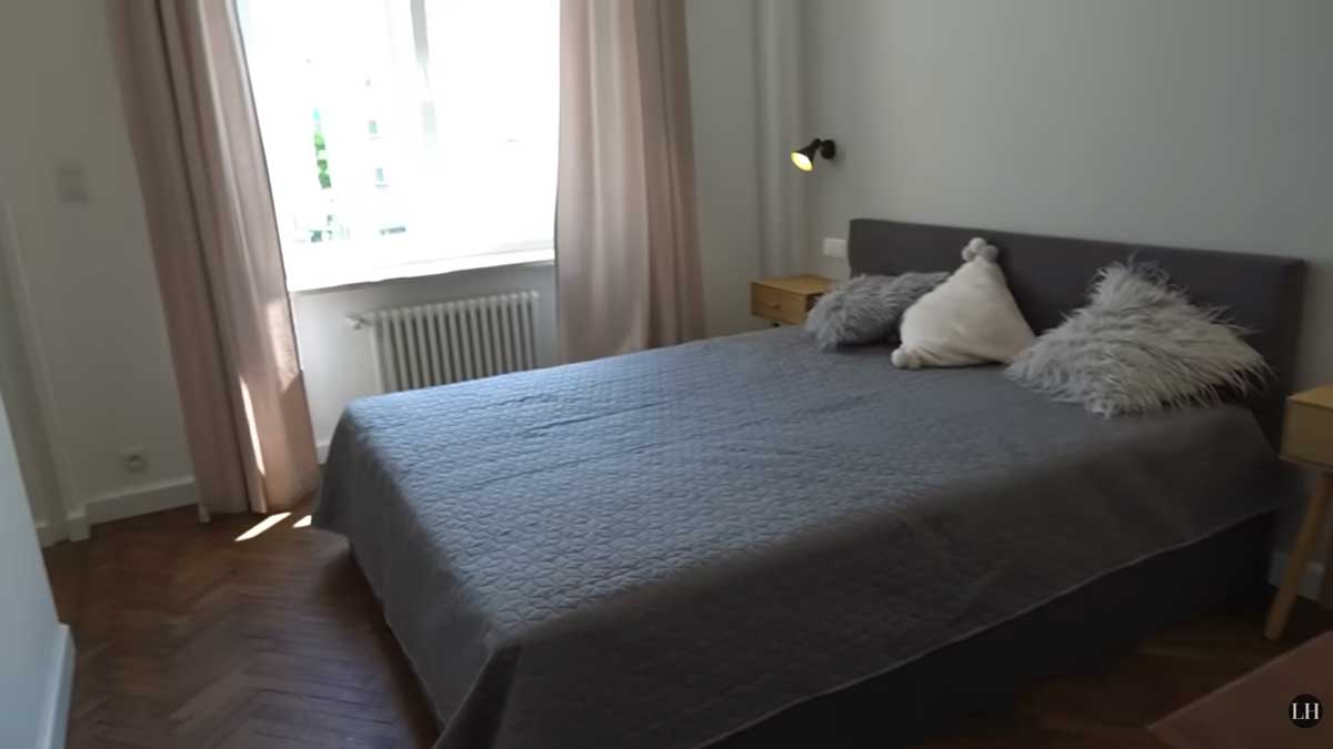 Ložnice po rekonstrukci s velkou postelí, světlými závěsy a renovovanými parketami.