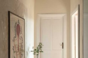 Úzká chodba s dřevěnou podlahou a obrazem na stěně doplněná pokojovou rostlinou.