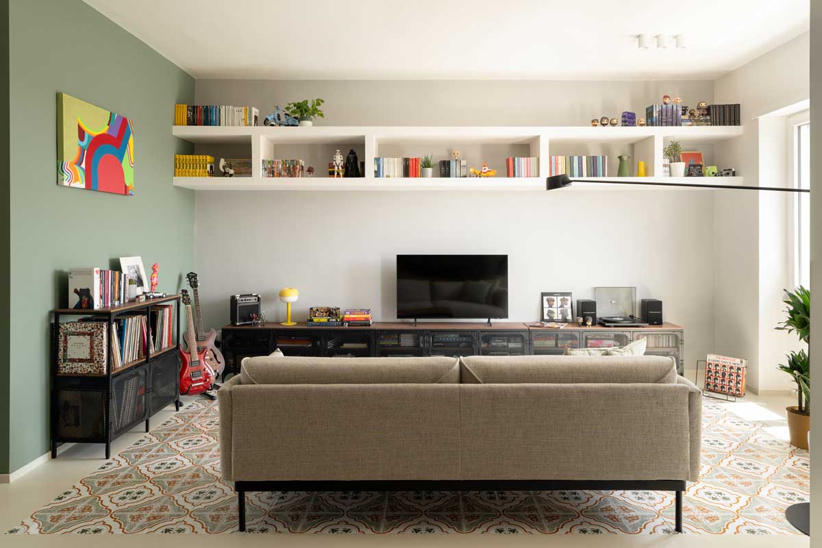 Obývací pokoj s historickou majolikovou dlažbou otevřený do denní zóny doplněný policemi s knihami vinylovými deskami a hudebními nástroji.