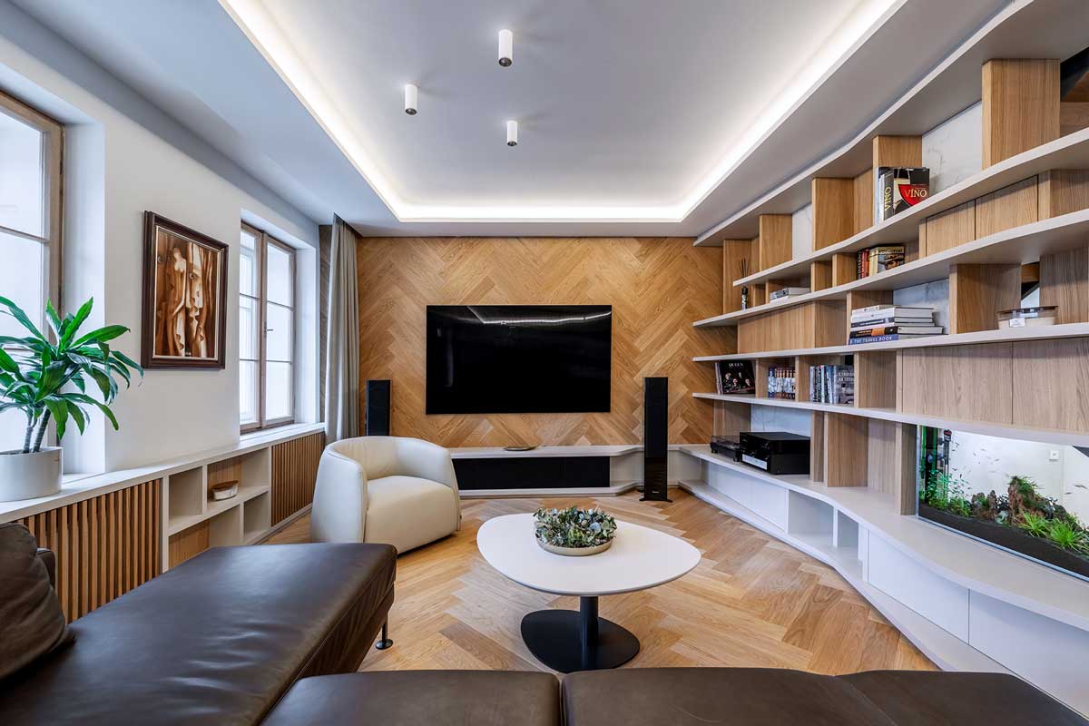 Obývací pokoj s velkoformátovou televizí dřevěnou stěnou ve vzoru stromečku a knihovnou vyrobenou na míru.