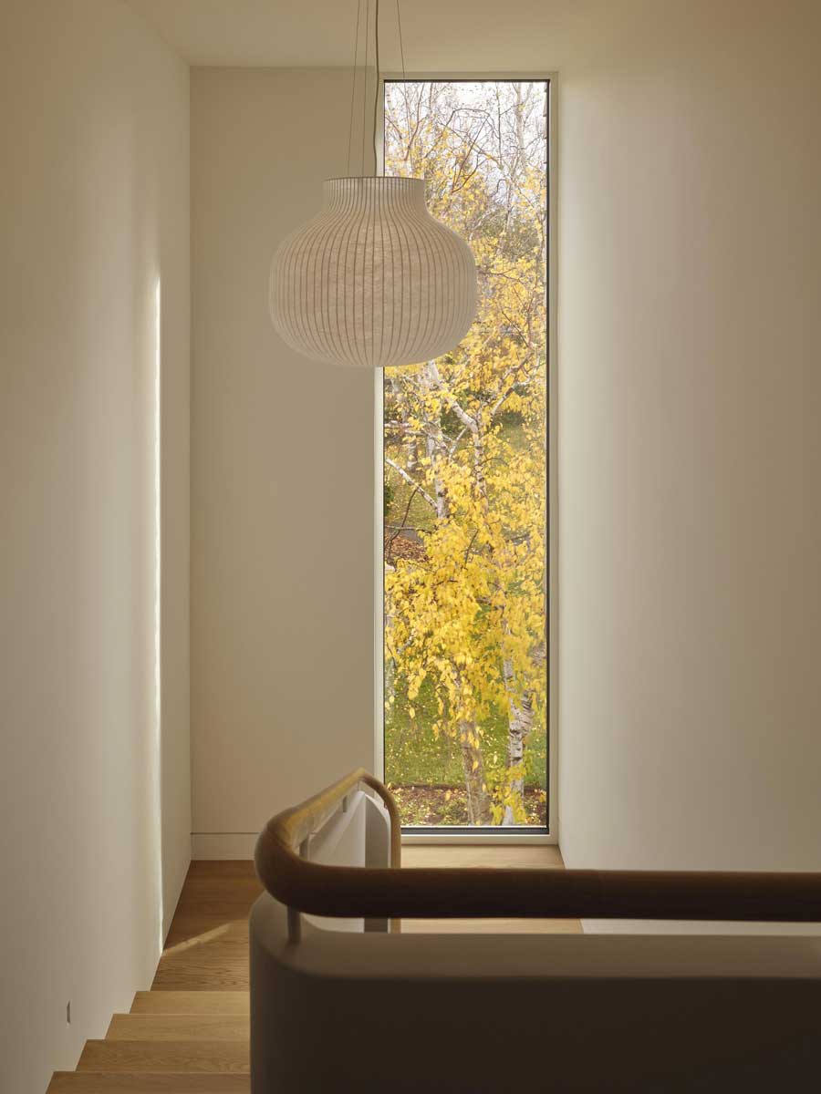 Dřevěné schodiště s velkým oknem propojuje interiér s venkovní scenérií a přivádí dovnitř světlo