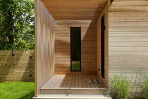 Dřevěná pergola u vstupu do domu vytváří polostín a zajímavou hru světla na fasádě.