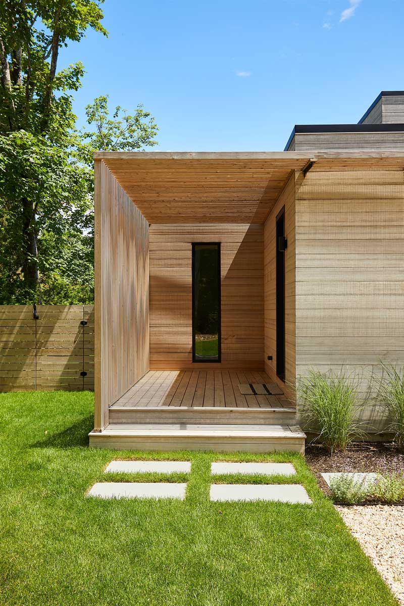 Dřevěná pergola u vstupu do domu vytváří polostín a zajímavou hru světla na fasádě.