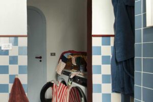 Koupelna s modrobílými obklady a obloukovým průchodem vedoucím do malé prádelny s pračkou a sušičkou.