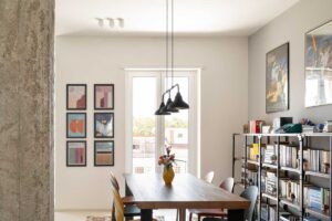 Jídelna s velkým dřevěným stolem barevnými židlemi a historickou dlažbou která vymezuje prostor v otevřeném interiéru.