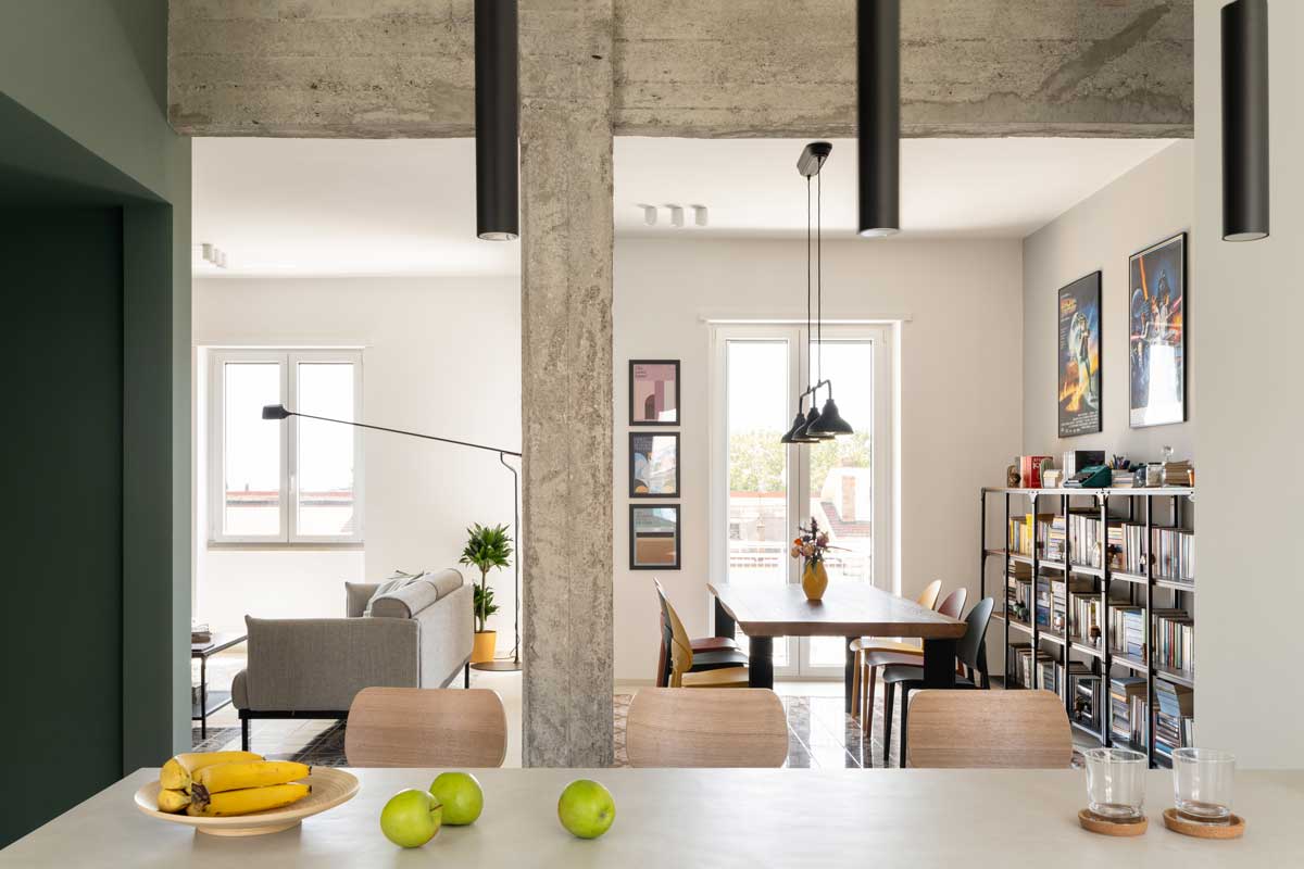 Pohled z kuchyňského ostrůvku do otevřené denní zóny kde se setkává jídelna obývací pokoj a přiznaná betonová konstrukce.