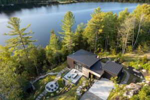 Letecký pohled na dům ve svahu u jezera obklopený lesem a terasami.