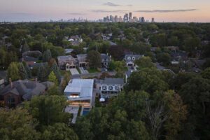 Letecký pohled na moderní dům zasazený do zelené čtvrti s panoramatem Toronta v dálce