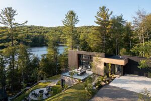 Moderní dům na svahu s terasou a výhledem na jezero a okolní lesy.