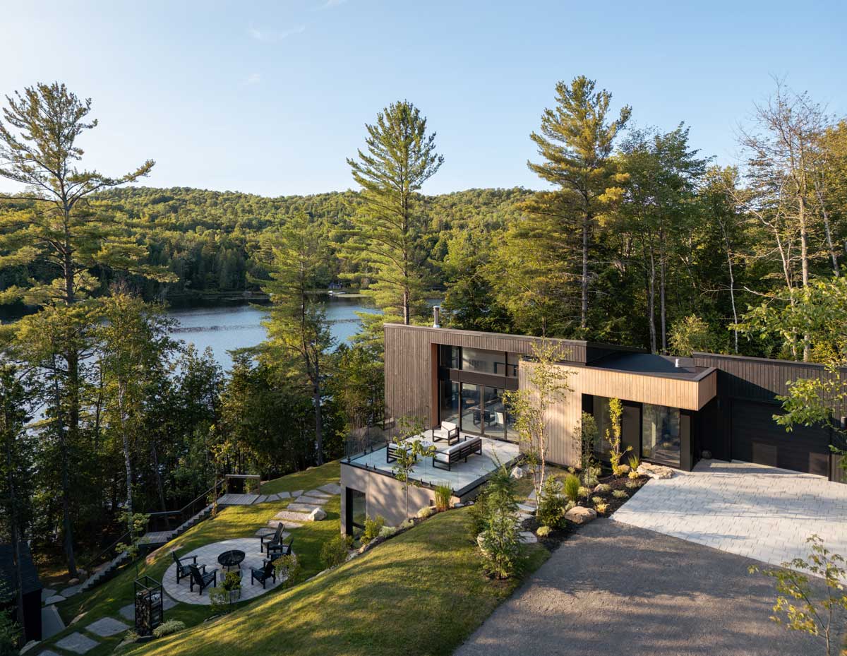 Moderní dům na svahu s terasou a výhledem na jezero a okolní lesy.