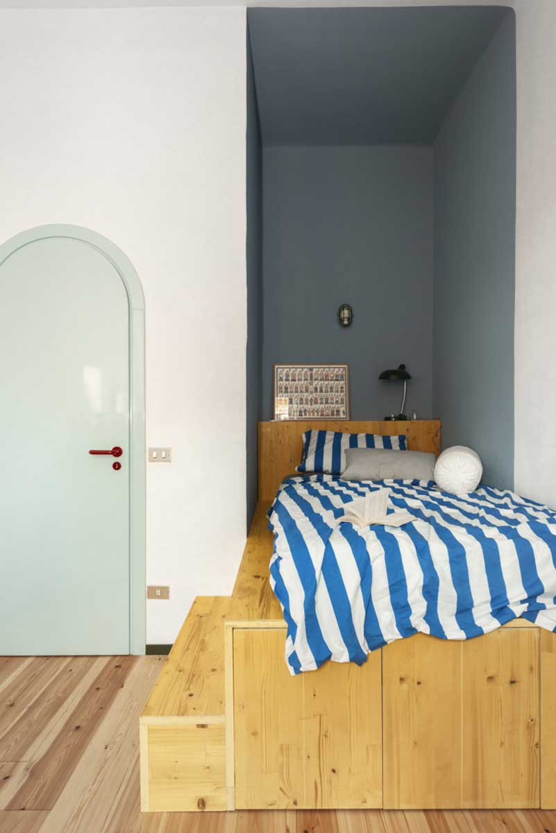 Malý pokoj s postelí z masivního dřeva umístěnou ve výklenku a modrou stěnou v pozadí.