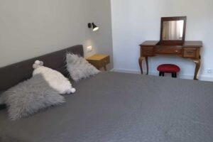 Ložnice po rekonstrukci s jednoduchou postelí, nočními stolky a elegantním toaletním stolkem z tmavého dřeva.