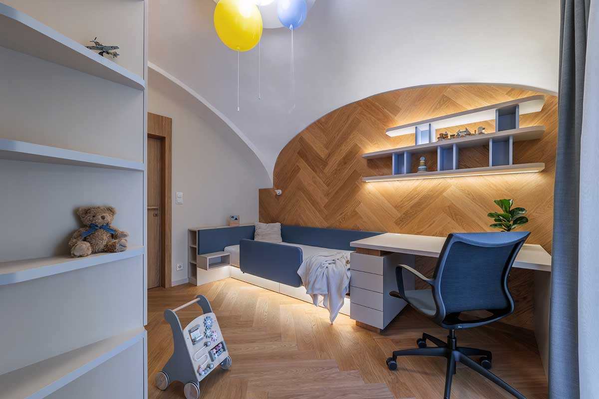 Dětský pokoj s oblou klenbou vestavěným nábytkem a pracovním koutem podsvíceným teplým světlem.