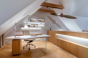 Pracovna v podkroví s historickou dřevěnou vrtulí zavěšenou pod krovem a nábytkem vyrobeným na míru.