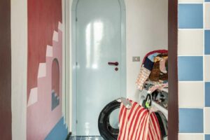 Úzká prádelna s modrou dlažbou a ručně malovanou nástěnnou dekorací na stěně.