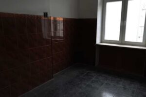 Původní kuchyně s tmavými obklady a oknem do dvora před zásadní proměnou dispozice bytu.