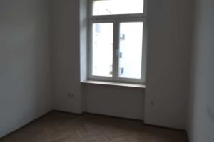 Prázdný pokoj s původními parketami a velkým oknem před začátkem rekonstrukce.