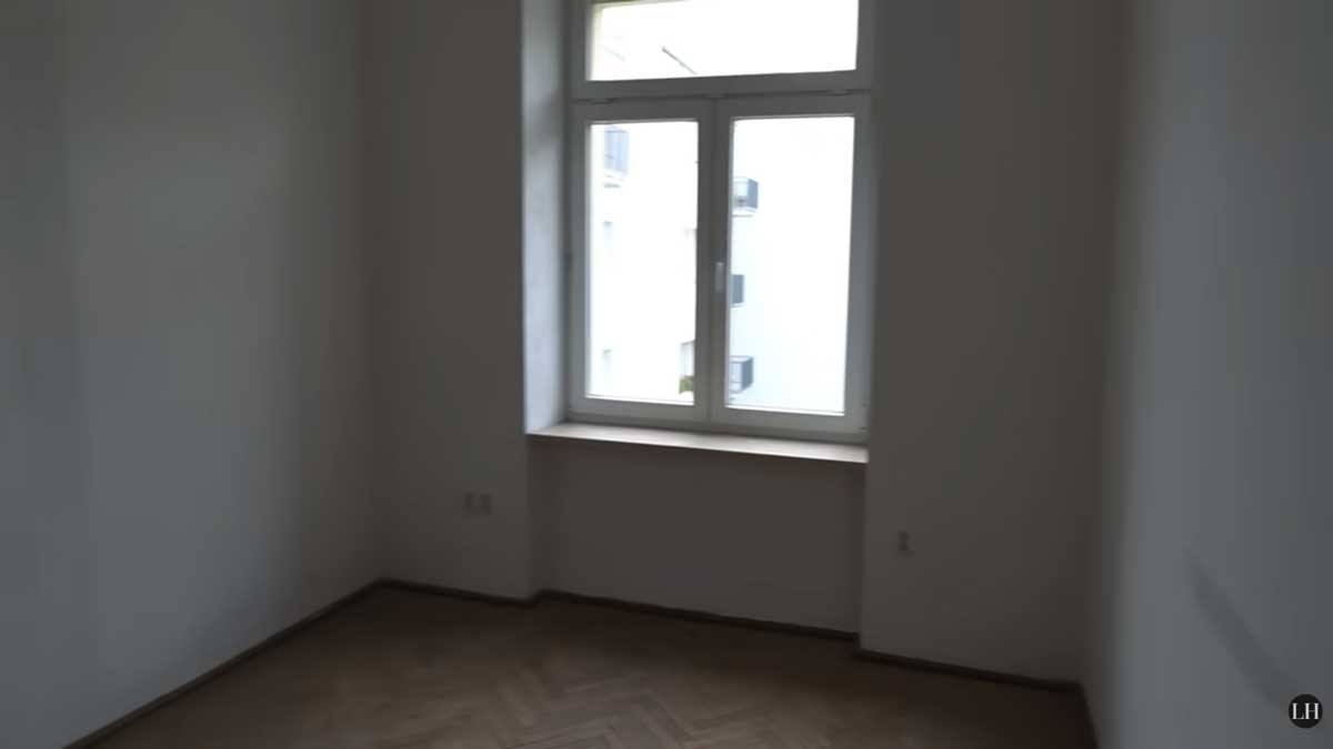 Prázdný pokoj s původními parketami a velkým oknem před začátkem rekonstrukce.