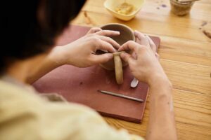 Keramik tvaruje hrnek z hlíny na pracovním stole a ručně připevňuje jeho ucho.