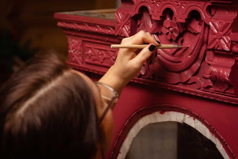 Restaurátorka pečlivě natírá zdobený kus nábytku a zvýrazňuje jeho ručně vyřezávané ornamenty.