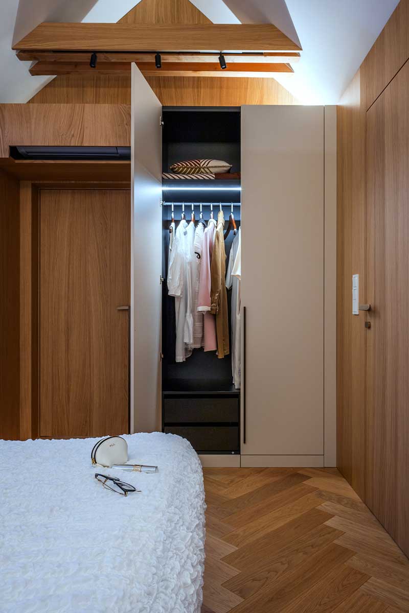 Vestavěná šatní skříň v ložnici s béžovými dvířky přírodní dýhou a vnitřním podsvícením.