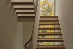 Vysoké okno na schodišti přivádí do interiéru světlo a nabízí výhled na okolní stromy