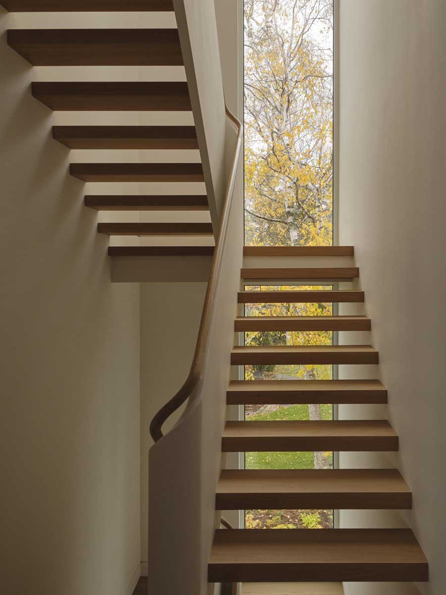 Vysoké okno na schodišti přivádí do interiéru světlo a nabízí výhled na okolní stromy