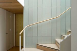 Schodiště s dřevěnými stupni a jemně zakřiveným zábradlím zasazené do minimalistického interiéru
