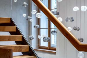 Dřevěné schodiště s proskleným zábradlím a ručně foukanou skleněnou plastikou připomínající mračna zavěšenou v prostoru.