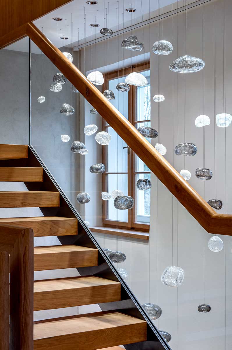 Dřevěné schodiště s proskleným zábradlím a ručně foukanou skleněnou plastikou připomínající mračna zavěšenou v prostoru.