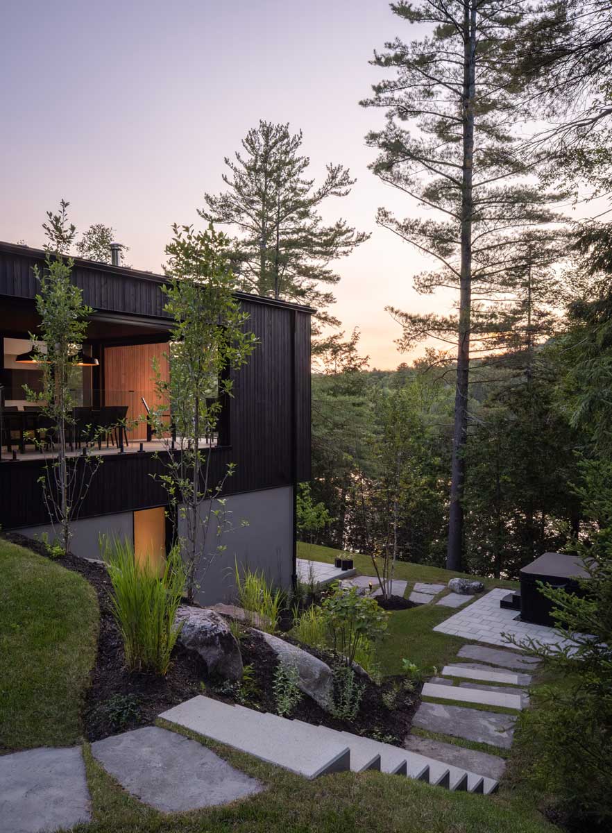 Kamenné schody a zahradní cesty na svažitém pozemku u domu obklopeného lesem.