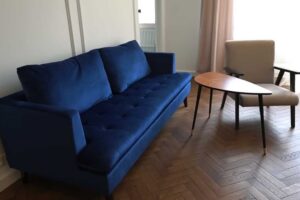 Obývací pokoj po rekonstrukci s modrou pohovkou, křeslem a renovovanými parketami v klasickém vzoru.