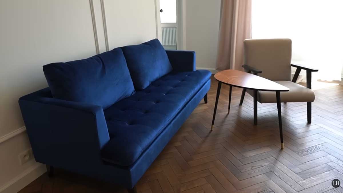 Obývací pokoj po rekonstrukci s modrou pohovkou, křeslem a renovovanými parketami v klasickém vzoru.