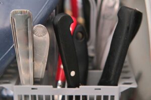 Příbory uložené v koši myčky rukojetí nahoru pro bezpečnější a hygieničtější manipulaci.