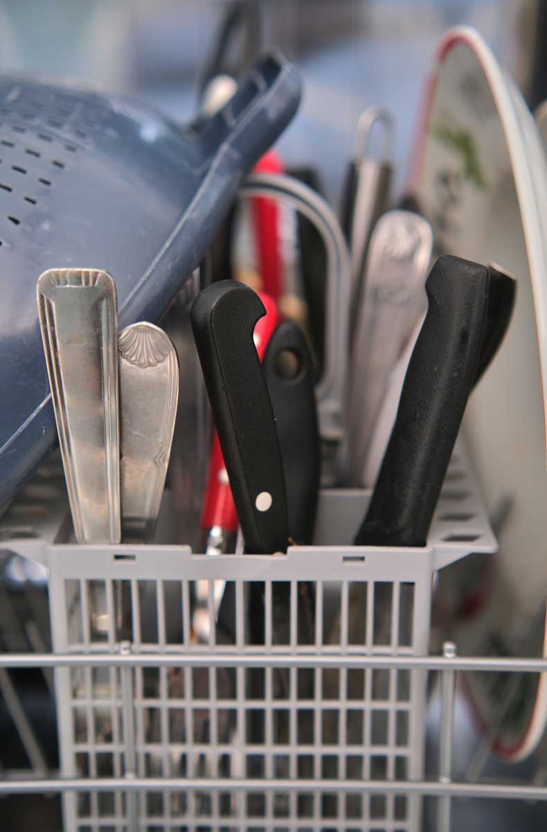 Příbory uložené v koši myčky rukojetí nahoru pro bezpečnější a hygieničtější manipulaci.
