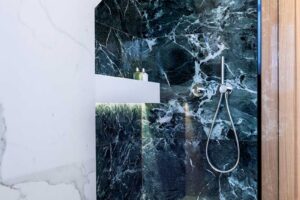 Sprchový kout s výrazným keramickým obkladem v dekoru tmavého kamene a minimalistickými sanitárními prvky.