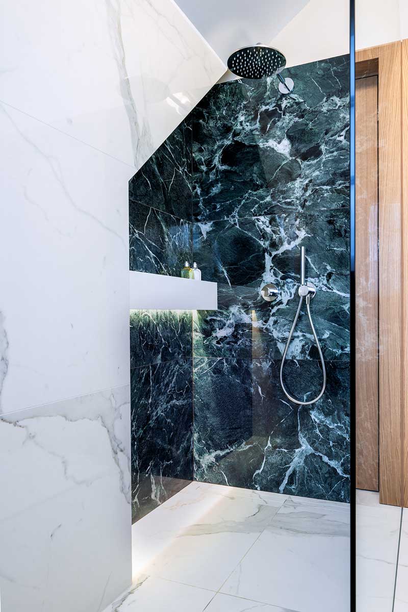 Sprchový kout s výrazným keramickým obkladem v dekoru tmavého kamene a minimalistickými sanitárními prvky.