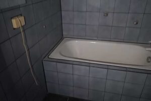 Malá koupelna s vanou a tmavými obklady působila před rekonstrukcí velmi uzavřeně a neprakticky.