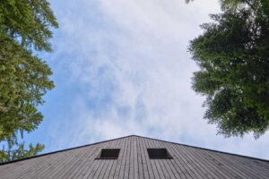 Pohled na dřevěný štít chalupy zespodu mezi korunami stromů