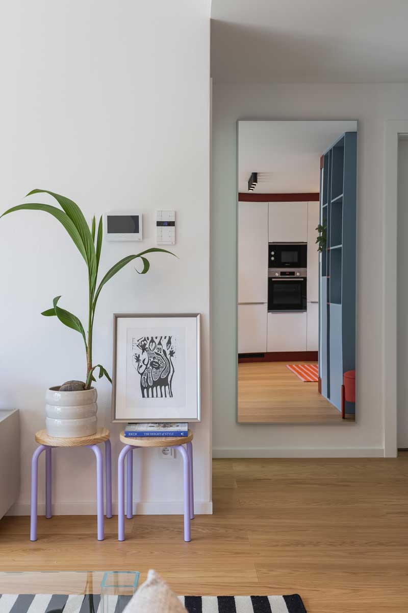 Dekorativní kout s pokojovou rostlinou, drobnými stolky a velkým zrcadlem vytváří u vstupu klidnou kompozici.