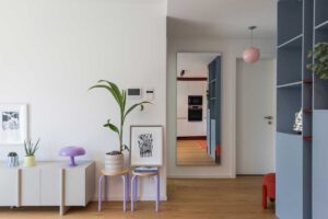 Nízká komoda a malé stolky s rostlinou a lampou vytvářejí u vstupu do bytu lehkou a hravou kompozici.